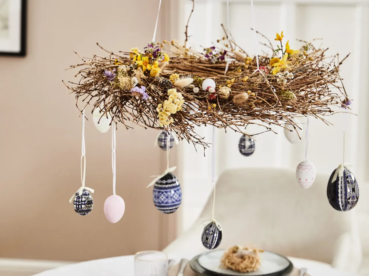 Wianek z gałązek ozdobiony suszonymi kwiatami i zawieszonymi pisankami. Inspirujące pomysły na dekoracje wielkanocne.