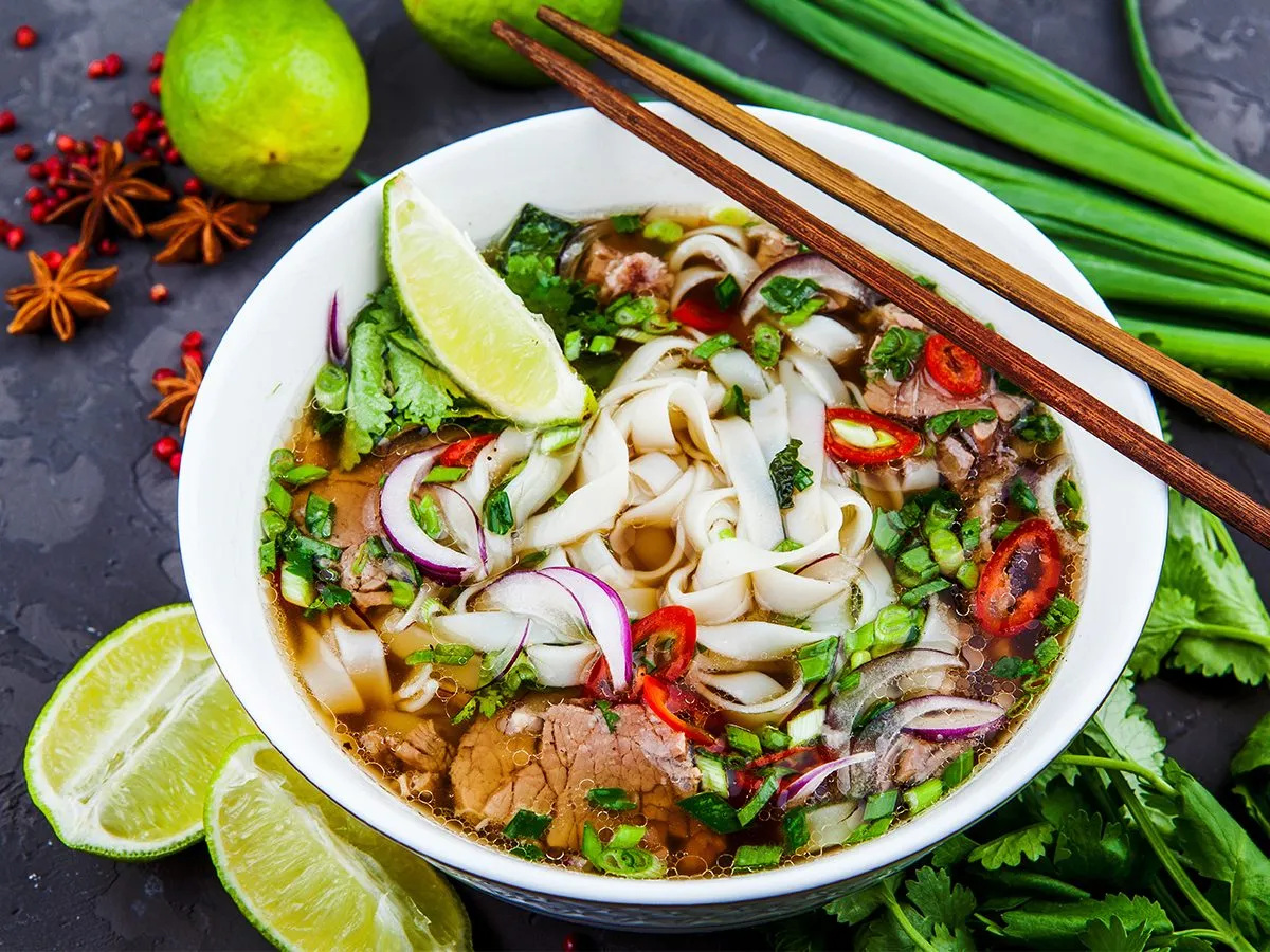 Aromaticzna zupa pho z wołowiną, makaronem ryżowym, cebulą, chili i limonką, ozdobiona szczypiorkiem i kolendrą.