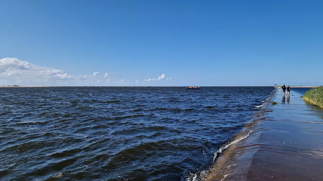 Spacer po molo, gdzie Wisła wpada do morza. Na wodzie łódź, na horyzoncie piasek i niebo.