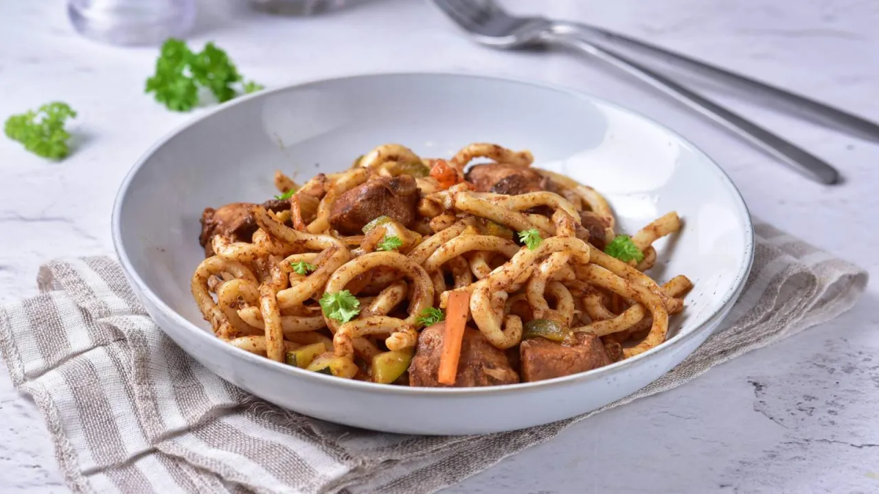 Pyszne udon z kurczakiem, warzywami i posiekaną natką pietruszki w białej misce.