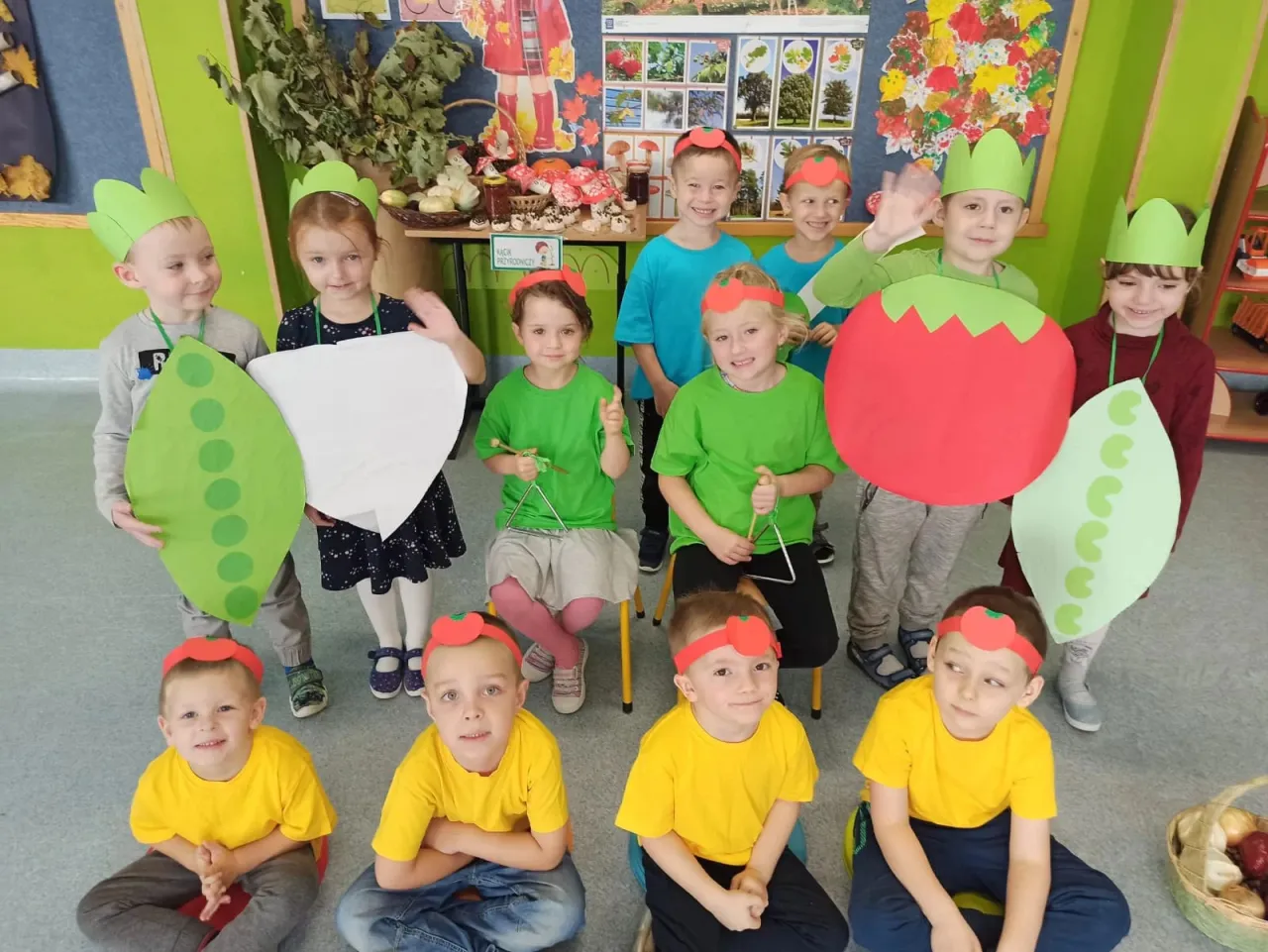 Dzieci w strojach warzyw, z zielonymi czepkami i rekwizytami. Wiersz o warzywach, gdzie pan pomidor jest gwiazdą.