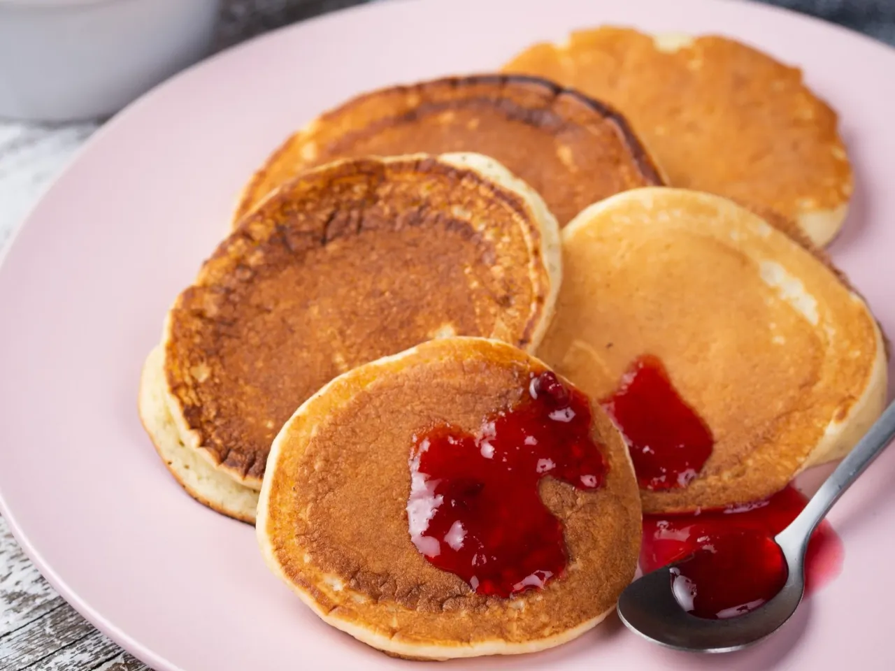 Szybki deser z niczego przepis: puszyste placuszki z dżemem malinowym na różowym talerzu.