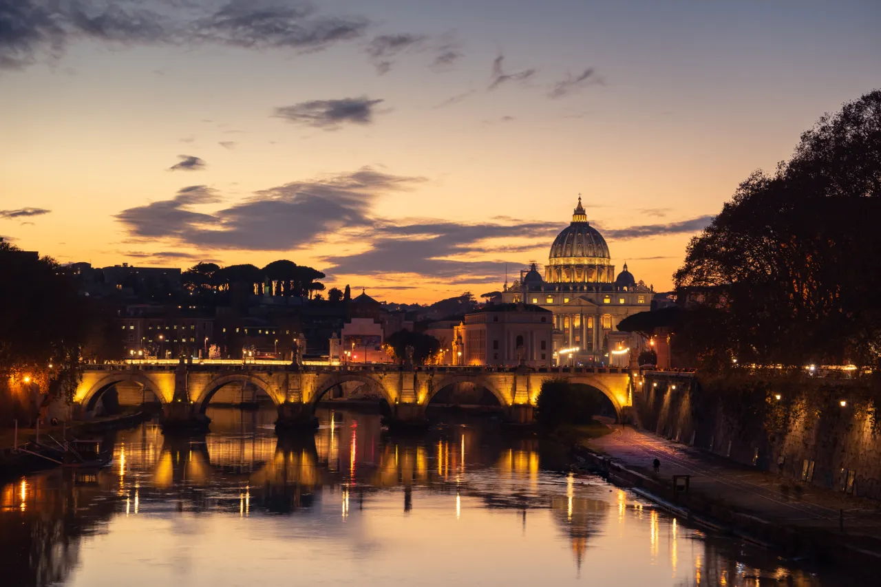 Zach&oacute;d słońca nad Tybrem, z Bazyliką św. Piotra w tle. Idealne miejsce na nocleg w Rzymie, gdzie najlepiej podziwiać takie widoki.