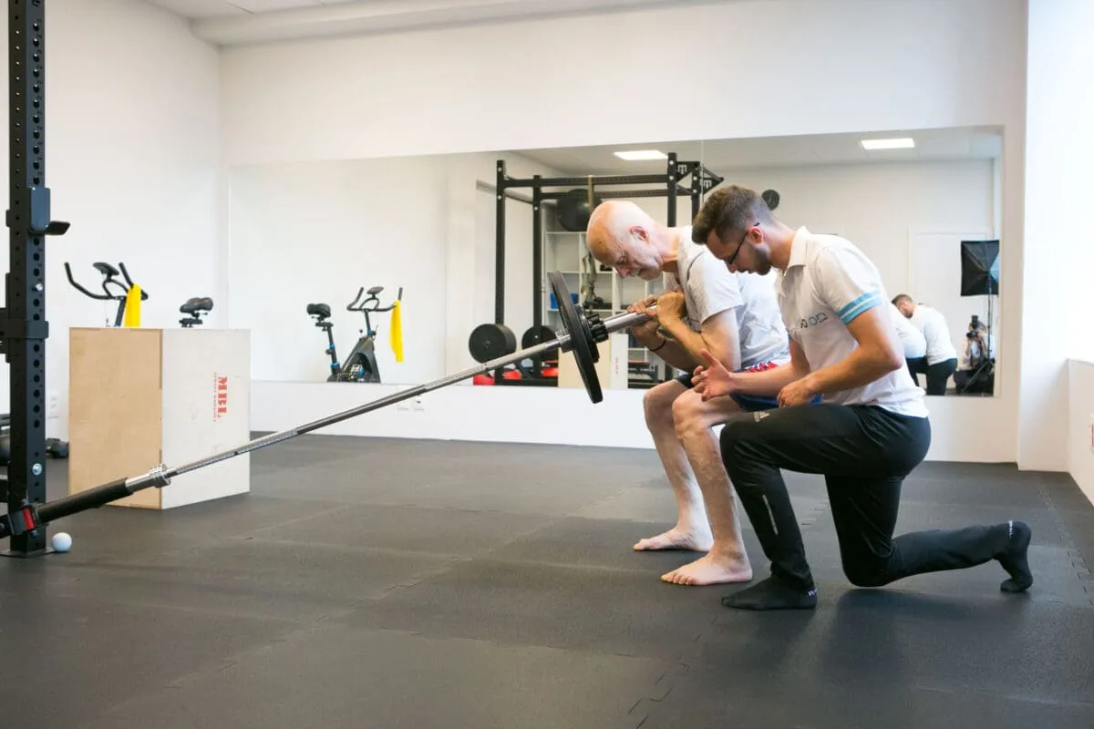 Starszy mężczyzna ćwiczy z fizjoterapeutą, kt&oacute;ry pokazuje mu prawidłowe wykonanie ruchu. To przykład, co to jest fizjoterapia &ndash; wsparcie w powrocie do sprawności.