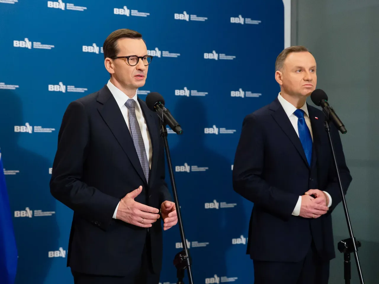 Mateusz Morawiecki i Andrzej Duda stoją przy mikrofonach. Andrzej Duda wzrostem przewyższa premiera.