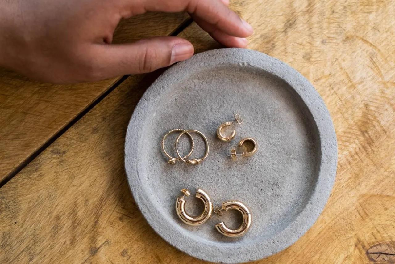 Dłoń przygotowuje złote kolczyki i pierścionki do czyszczenia biżuterii.