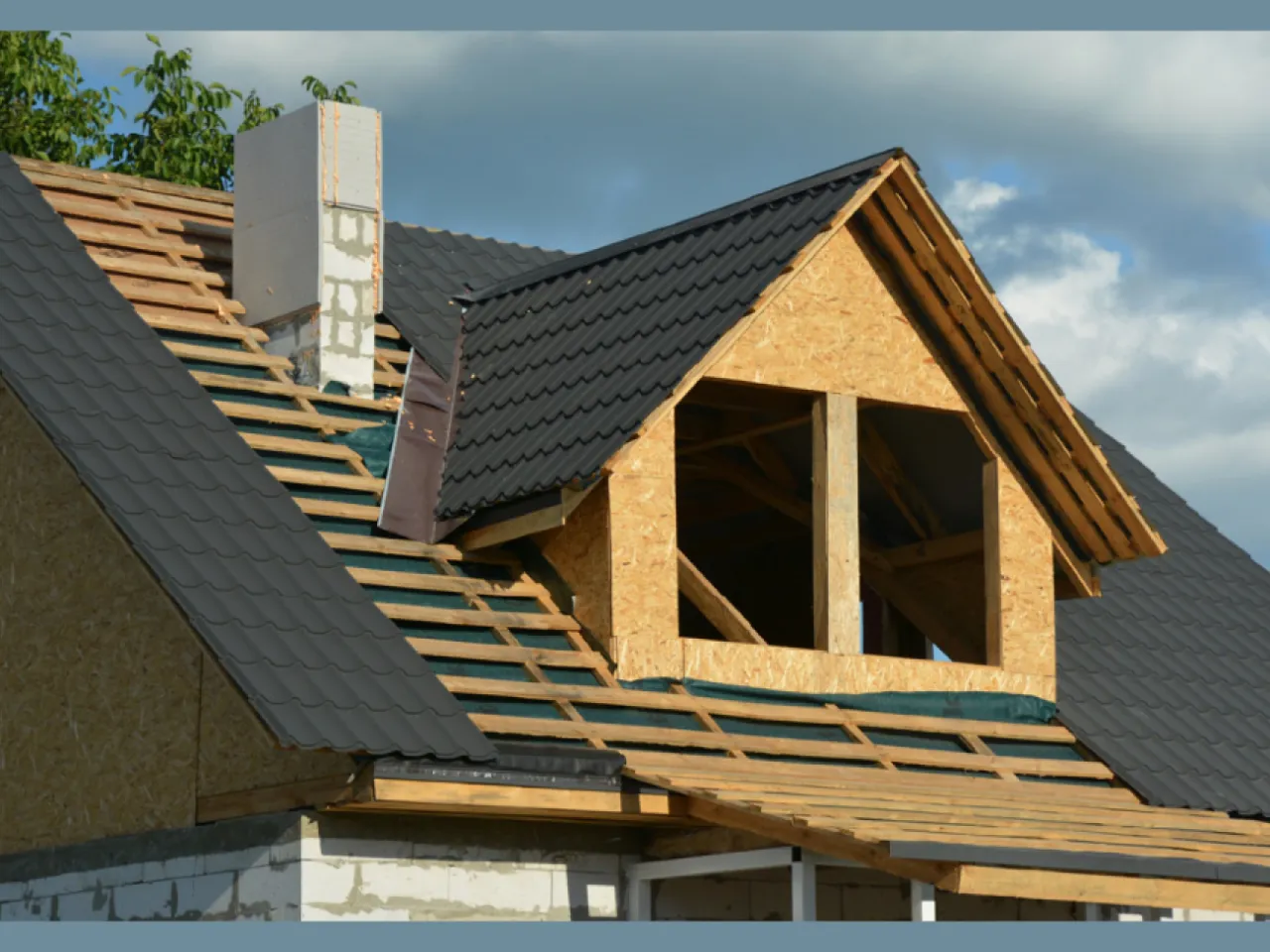 Budowa dachu: widoczny komin z cegły, przygotowania do obr&oacute;bki komina blachą, dach&oacute;wka i więźba dachowa.