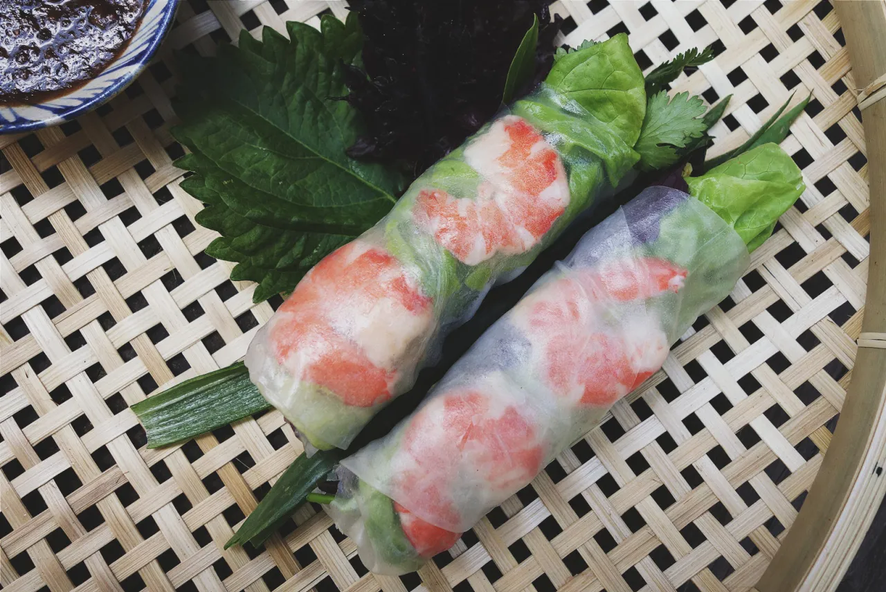 Jak zrobić papier ryżowy? Dwa świeże sajgonki z krewetkami i warzywami, podane na bambusowej macie.