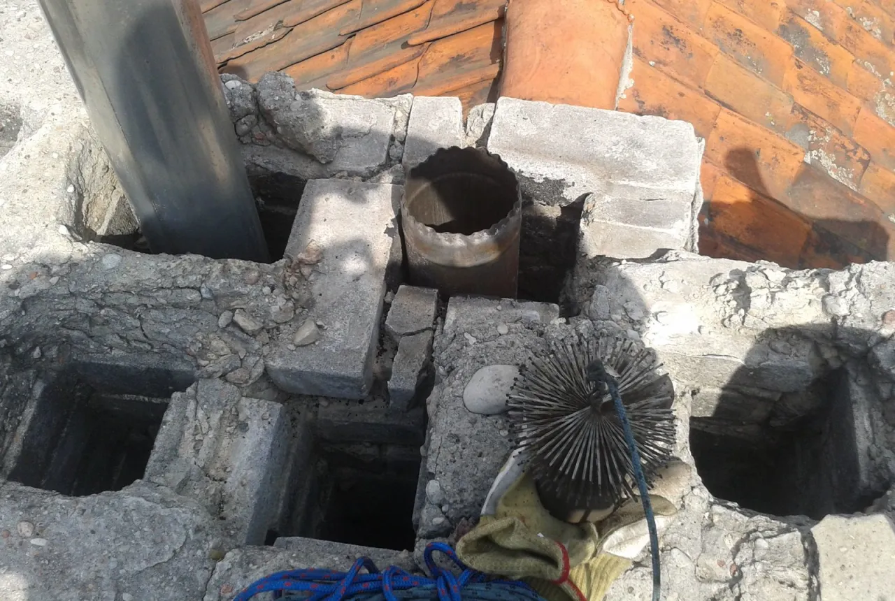 Uszkodzony komin, widoczne pęknięcia i luźne cegły. To mogą być objawy nieszczelności. Widoczna szczotka do czyszczenia.