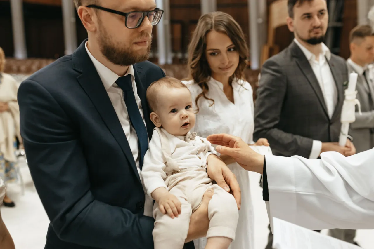 Rodzice trzymają dziecko do chrztu. Zastanawiasz się, ile kosztuje fotograf na chrzest?