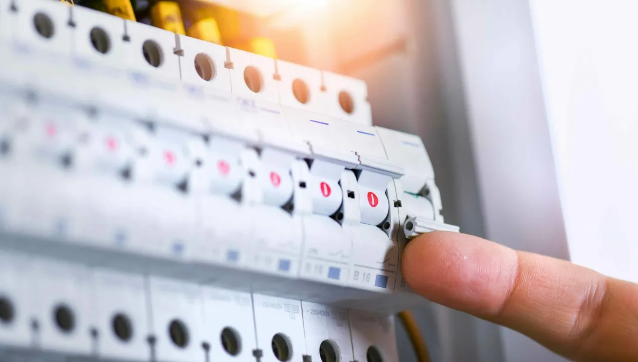 Palec naciska dźwignię wyłącznika, pokazując, jak włączyć bezpiecznik.