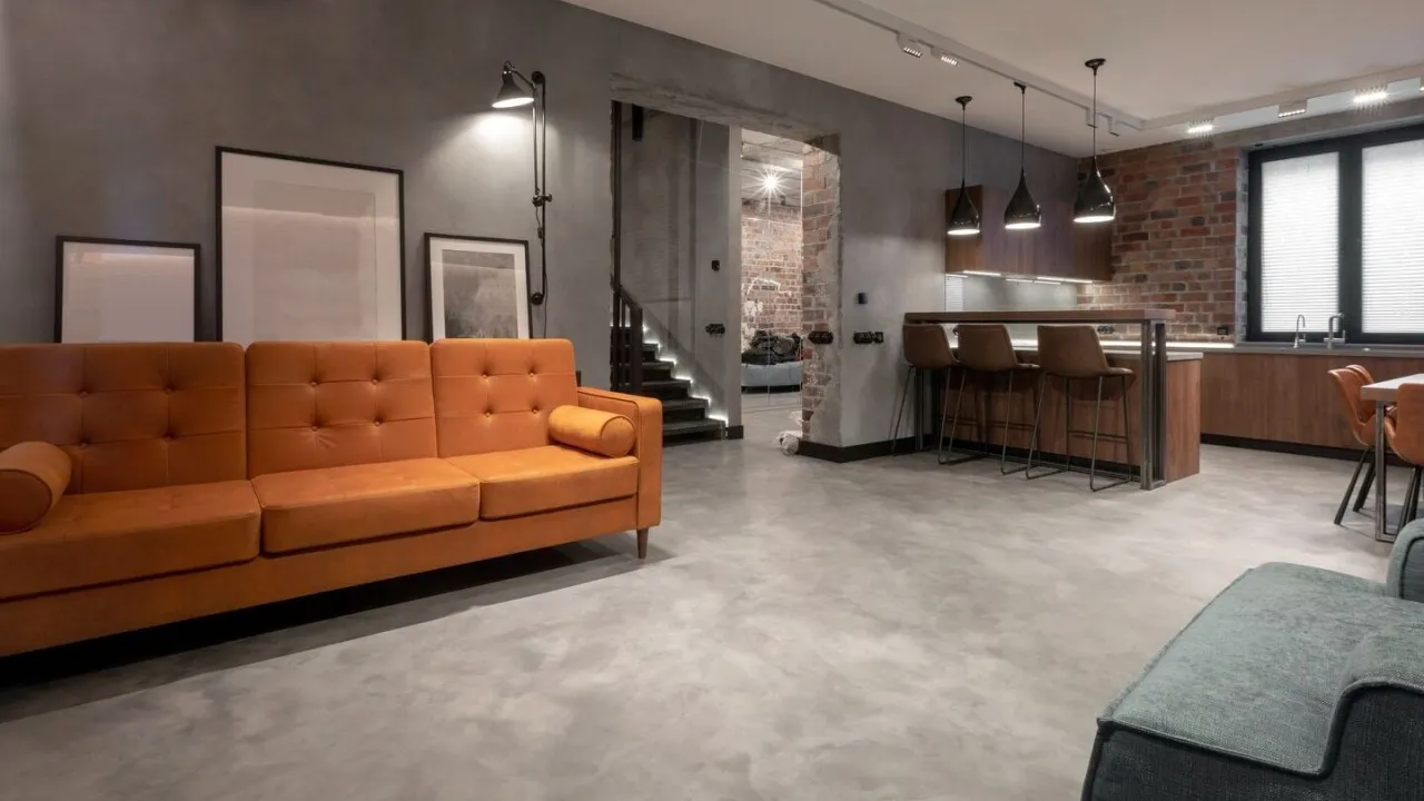 Nowoczesne wnętrze z pomarańczową kanapą i betonową podłogą. Dowiedz się, ile kosztuje położenie betonu dekoracyjnego.