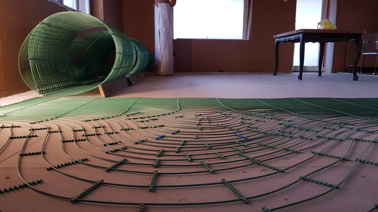 Zielone maty kapilarne rozłożone na podłodze, przygotowane do montażu ogrzewania podłogowego. W tle zielona rolka materiału.