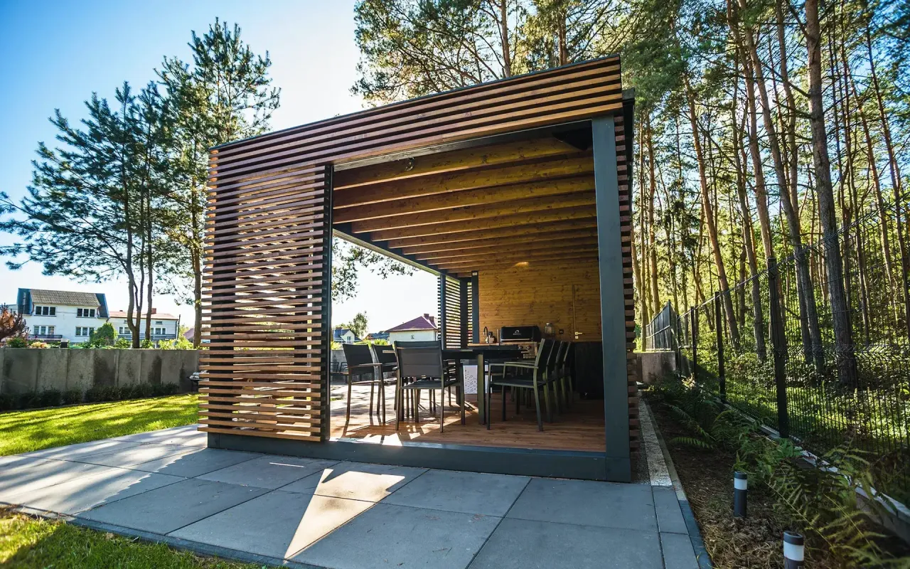 Nowoczesna altana z drewnianą zabudową, idealna na letnie wieczory. Stoły i krzesła czekają na gości.