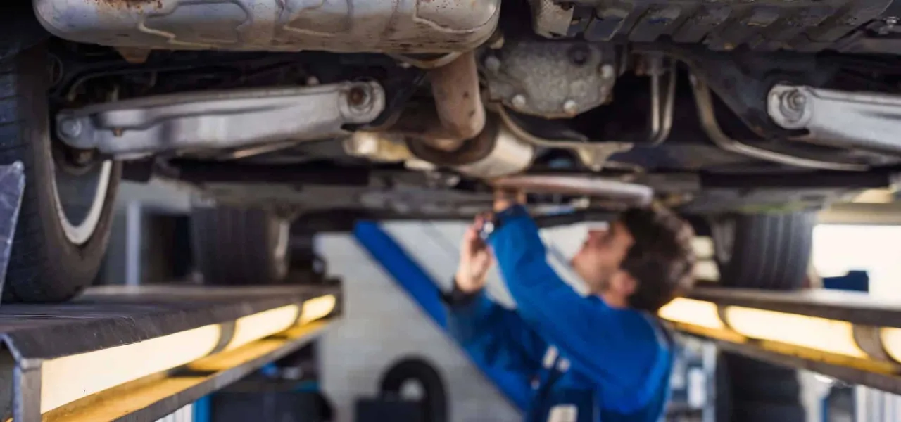 Mechanik sprawdza podwozie auta, zastanawiając się, ile kosztuje regeneracja maglownicy.