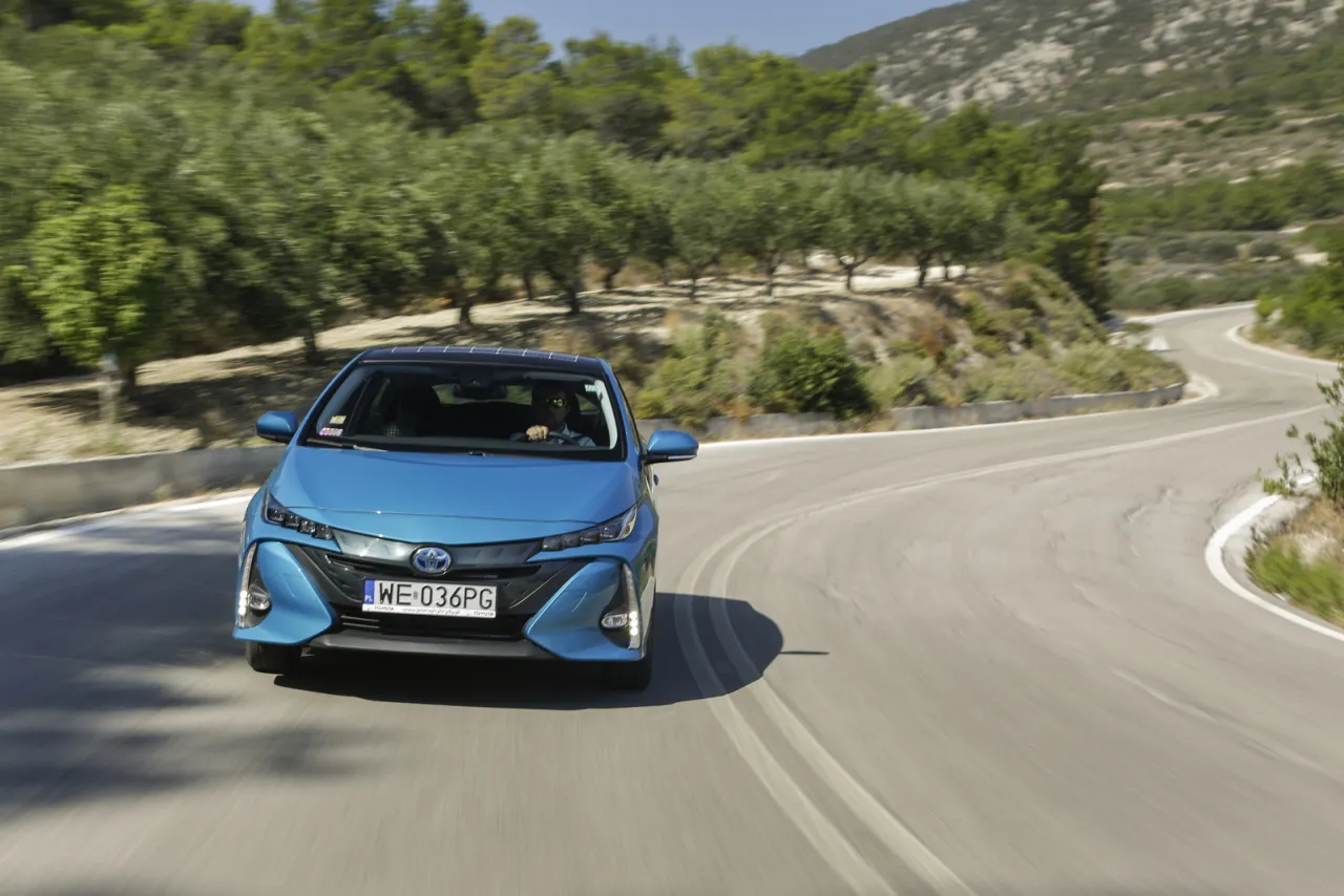 Niebieska Toyota Prius pokonuje kręty g&oacute;rski zakręt. Zastanawiasz się, ile pali Toyota Prius? Ten model jest znany z niskiego spalania.
