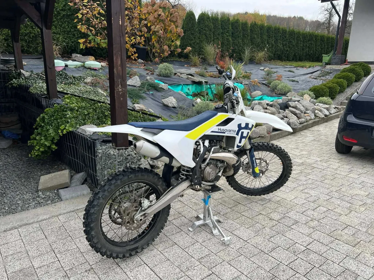 Husqvarna 250 cross na stojaku, gotowa do jazdy po jesiennym ogrodzie.