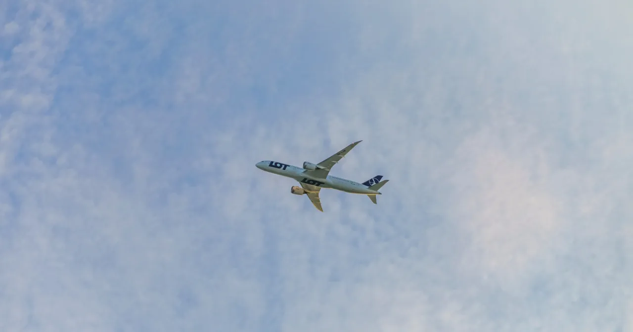 Samolot LOT leci przez chmury. Zastanawiasz się, ile trwa lot z Polski do Nowego Jorku?