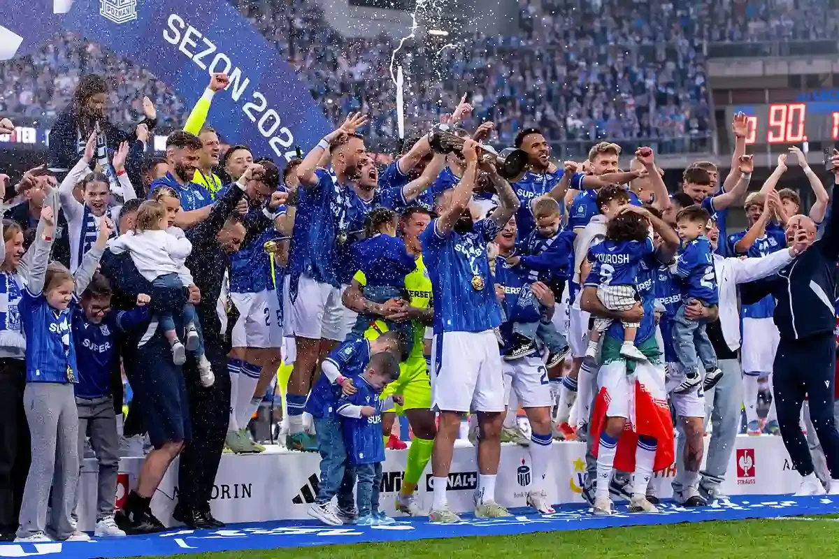 Radość piłkarzy i kibic&oacute;w świętujących awans do Ekstraklasy. Wszyscy w niebieskich strojach, w tle tłum i konfetti.