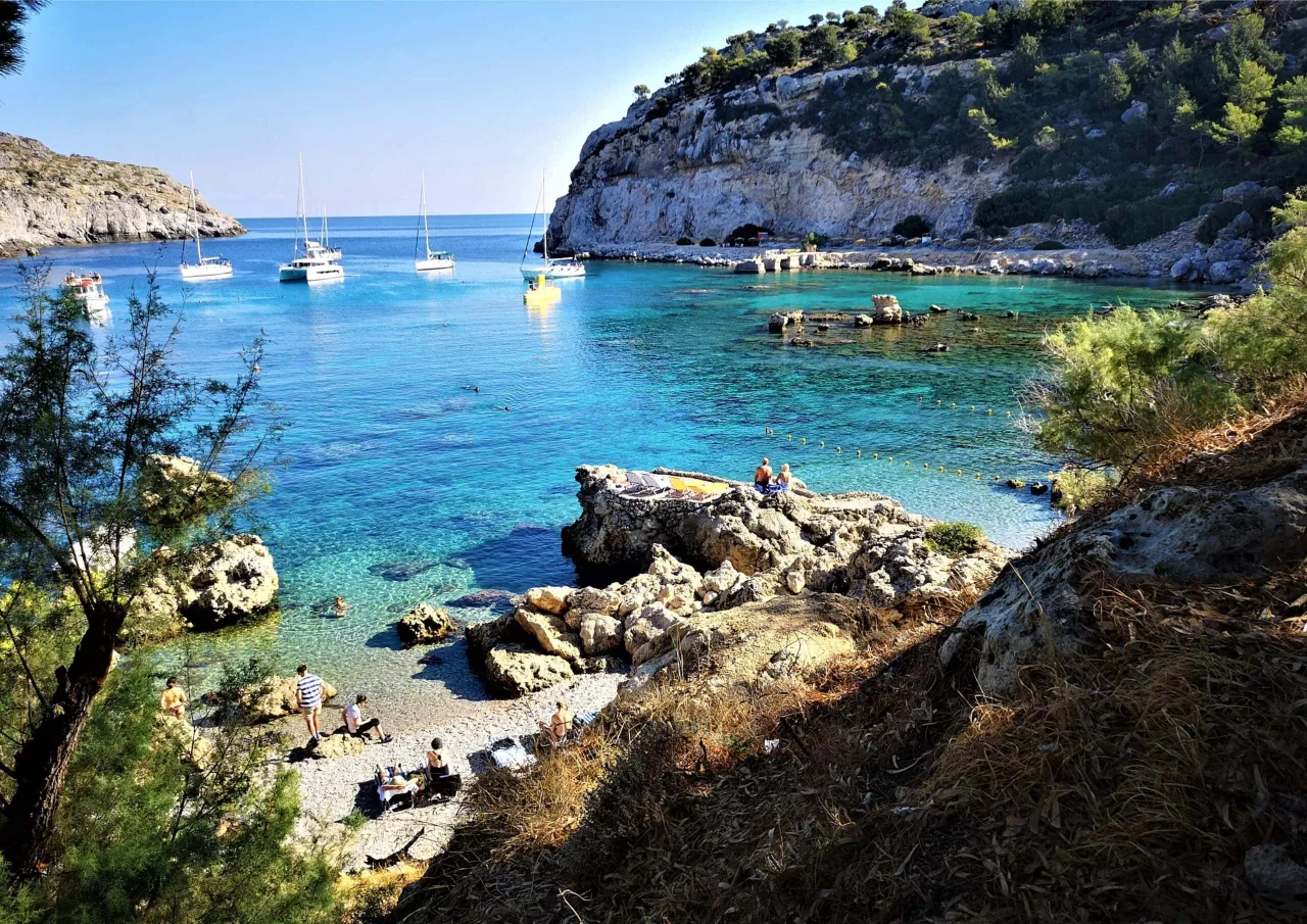 Zatoka z krystalicznie czystą wodą, łodziami i ludźmi odpoczywającymi na plaży. To jedno z rodos najpiękniejsze miejsca.