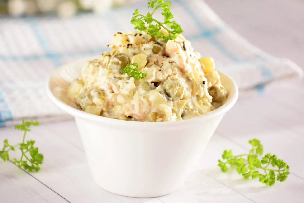 Pyszna sałatka jarzynowa w białej miseczce, udekorowana natką pietruszki. Idealna na każdą okazję.