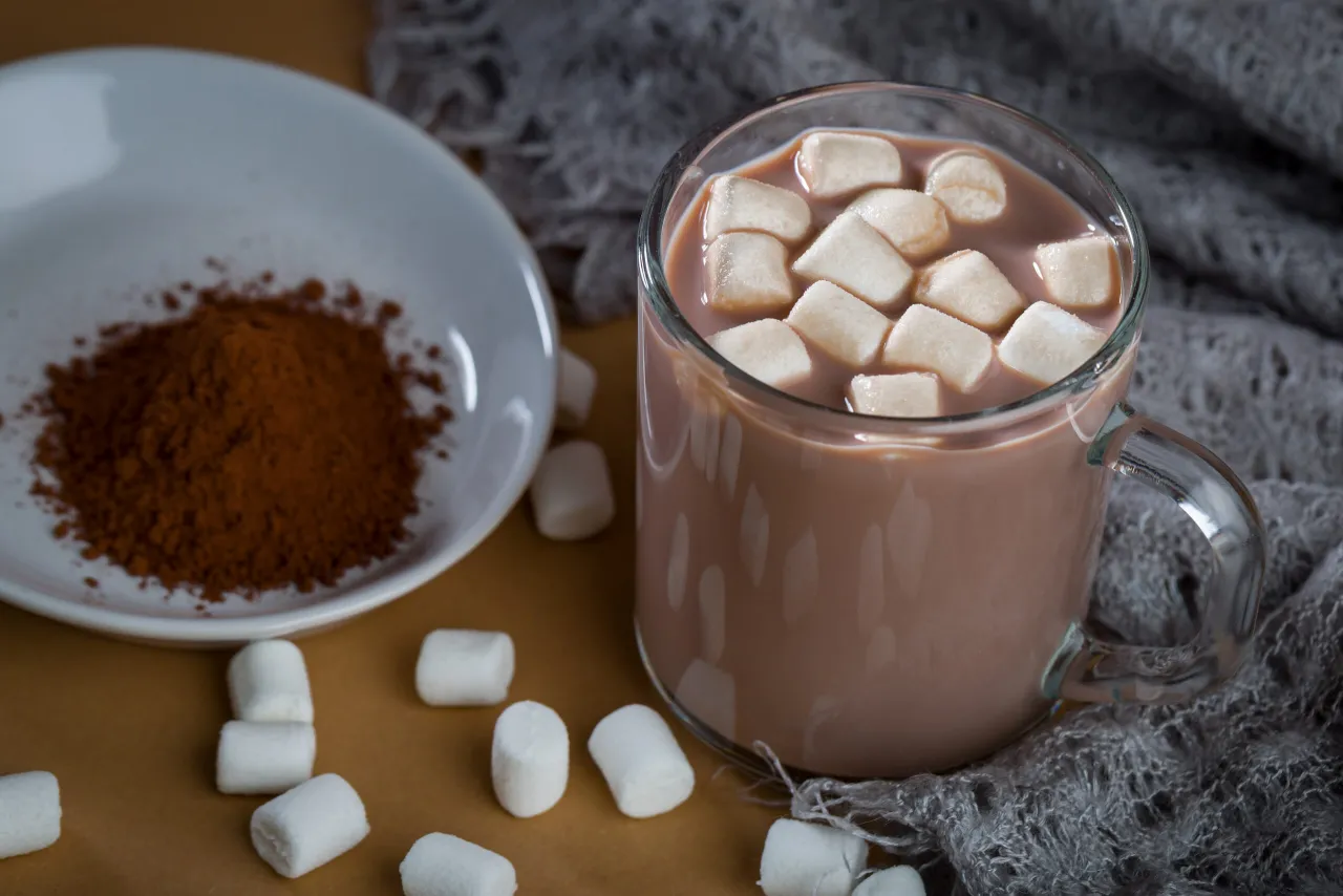 Jak zrobić kakao z wodą? Na talerzyku kakao, obok kubek gorącego napoju z piankami i marshmallow.