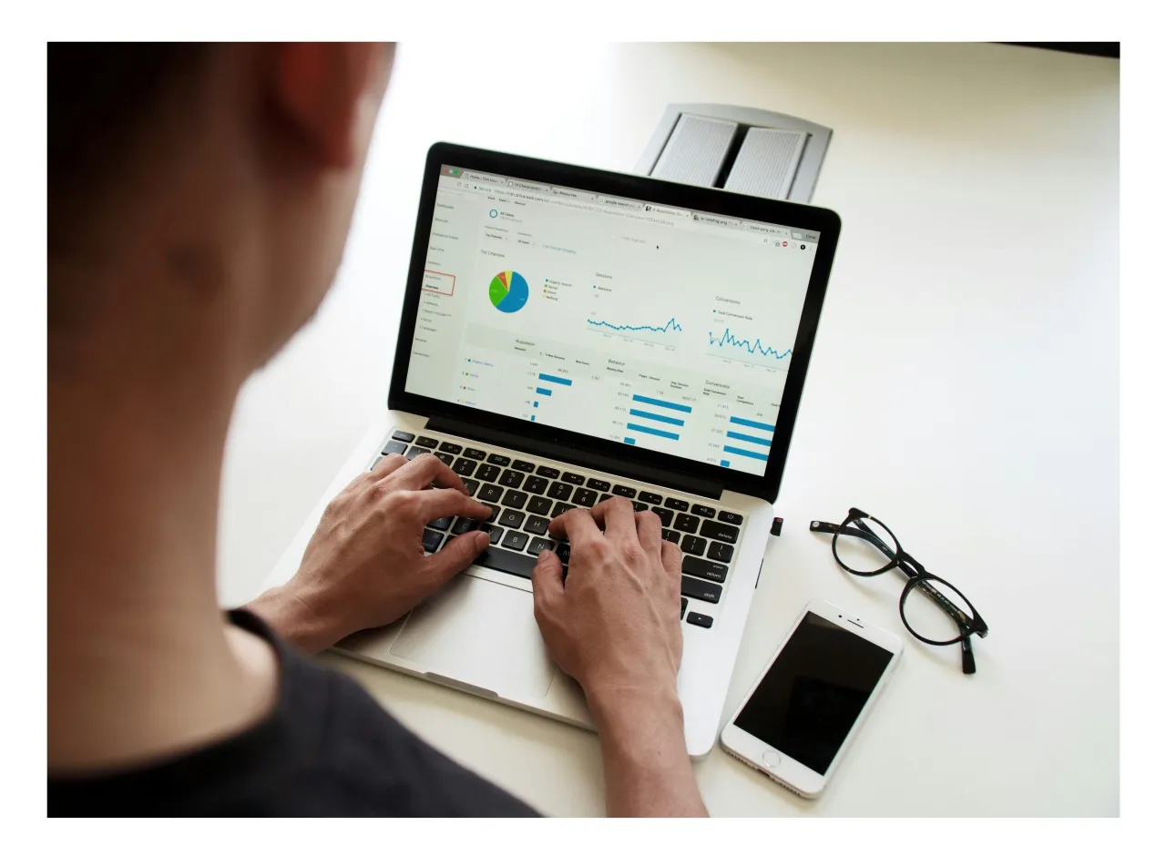 Osoba analizuje dane na laptopie, szukając sposob&oacute;w na poprawę wynik&oacute;w, być może unikając negatywnego SEO. Obok leżą okulary i smartfon.