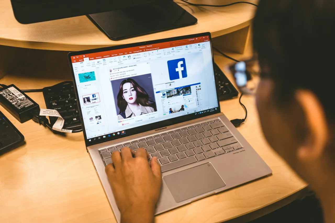 Person arbeitet am Laptop mit Facebook-Logo im Hintergrund