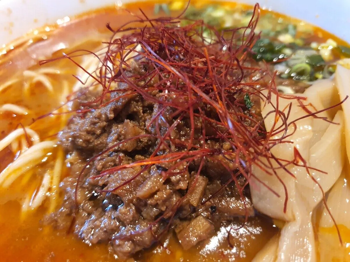 Miseczka aromatycznego ramen z mielonym mięsem w stylu bbq, posypana nitkami chili i kawałkami bambusa.