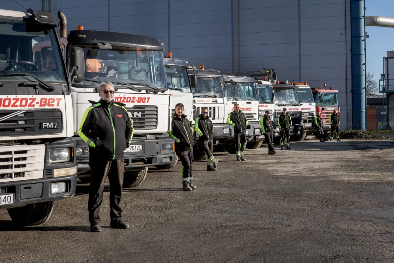 Grupa pracowników w odblaskowych kurtkach stoi przed rzędem betoniarek. Zapytaj o to, ile kosztuje metr sześcienny betonu.