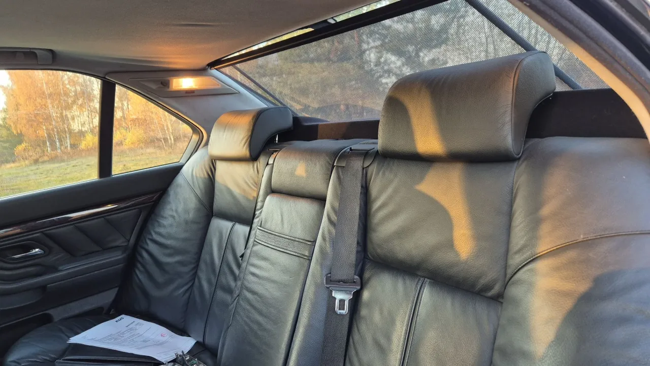 Sk&oacute;rzana tylna kanapa BMW E38 Long w jesiennym słońcu. Widok z wnętrza samochodu na jesienny krajobraz.