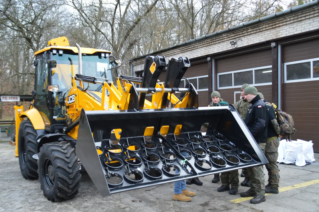 Żółta koparko-ładowarka JCB z zamontowanym osprzętem, obok stoją żołnierze. Ile waży koparko-ładowarka jcb?
