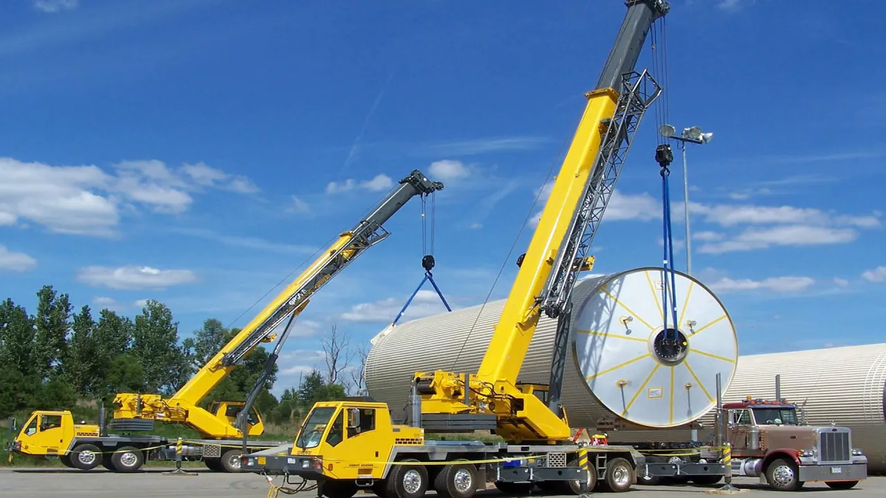 Dwa ż&oacute;łte dźwigi unoszą duży, cylindryczny element. To pokazuje, co to jest dźwig i jak potężne są te maszyny.