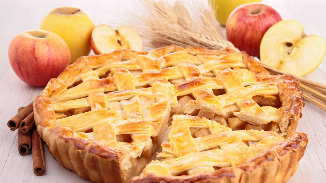 Złocista szarlotka z jabłkami i cynamonem, otoczona świeżymi owocami i kłosami zboża. Czy szarlotka jest zdrowa? Zależy od składników!
