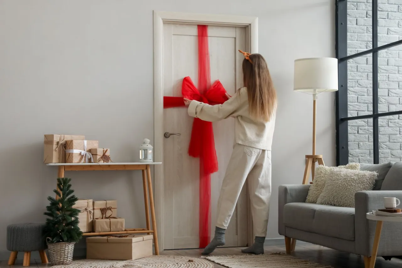 Dziewczynka tworzy wielką czerwoną kokardę na drzwiach, pokazując, jak zrobić kokardę na drzwi.