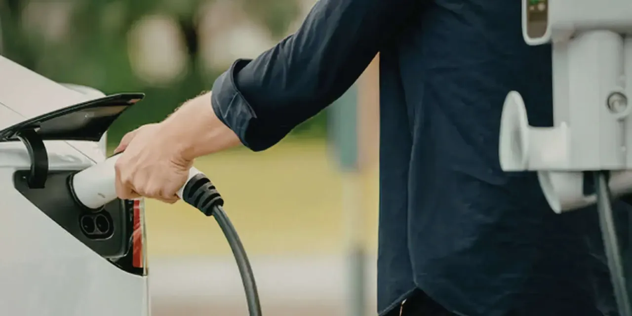 Mężczyzna podłącza białą wtyczkę do gniazda ładowania samochodu elektrycznego. To wygodne i ekologiczne rozwiązanie.