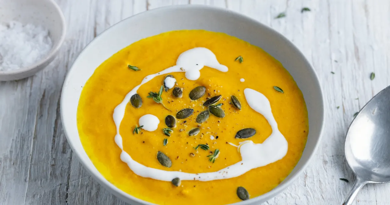 Aksamitna zupa z dyni wlasciwosci odżywcze. Kremowa, pomarańczowa zupa z pestkami dyni i ziołami, ozdobiona śmietaną.