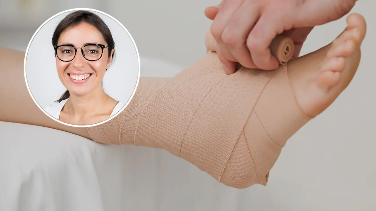 Uśmiechnięta kobieta w okularach patrzy na nogę z bandażem. Objawy skręconego stawu skokowego mogą być łagodzone przez odpowiednie opatrzenie.