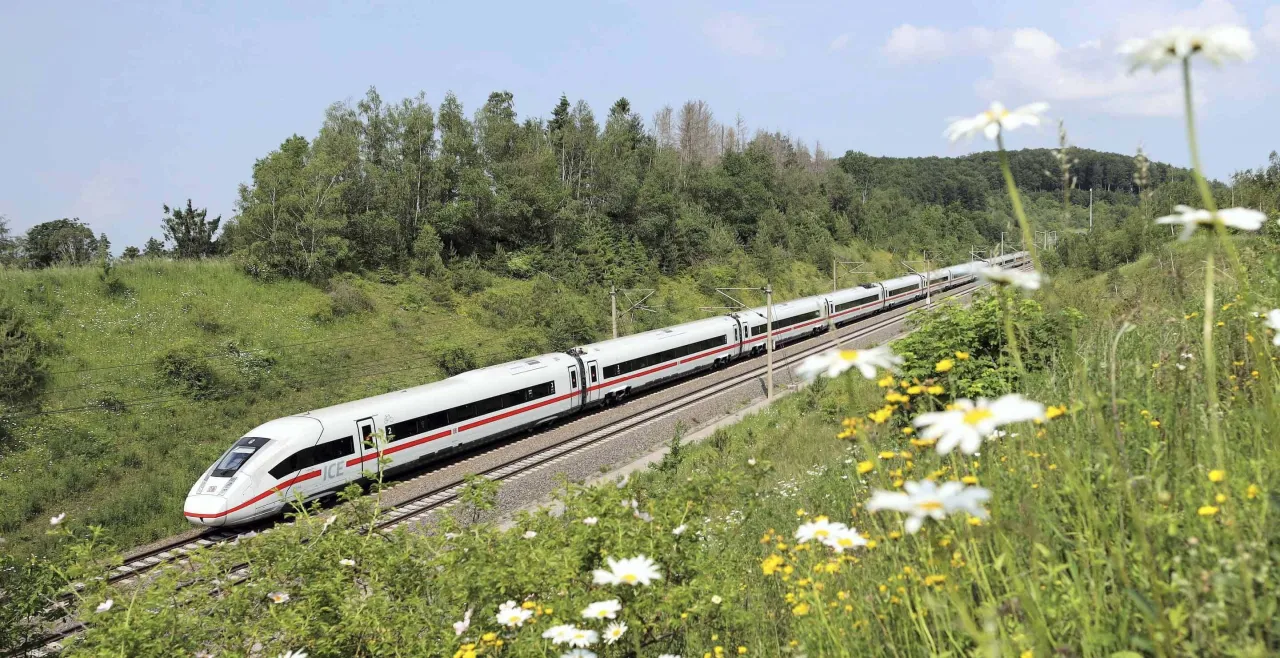Szybki pociąg ICE jedzie przez zielony krajobraz. Dowiedz się, jak kupić bilet na pociąg w Niemczech, by podr&oacute;żować tak komfortowo.