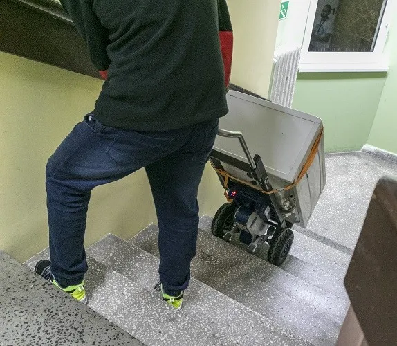 dwie osoby wnoszące duże urządzenie AGD po schodach