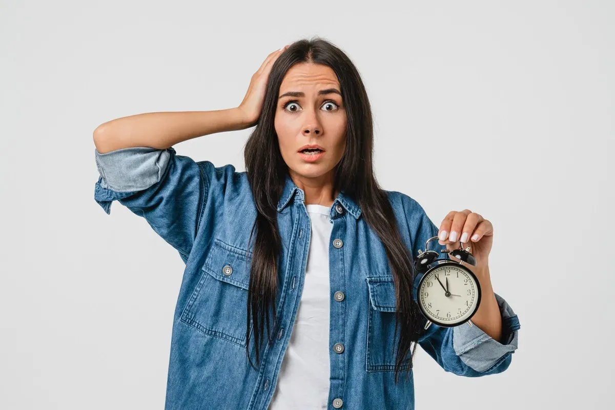 Przerażona kobieta z budzikiem w dłoni zastanawia się, czy wniosek o dofinansowanie do żłobka trzeba składać co miesiąc.