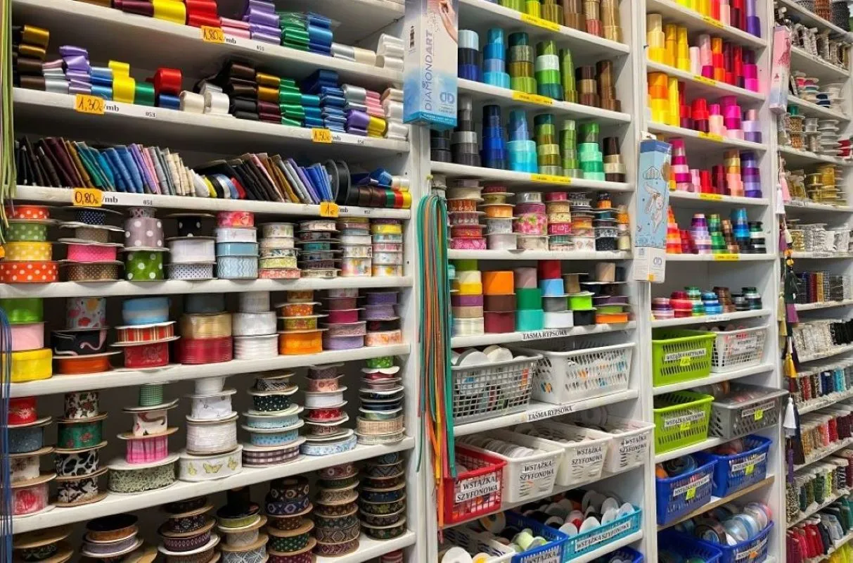 Kolorowe taśmy, wstążki i sznurki – wszystko, co kupujemy w pasmanterii, poukładane na półkach.
