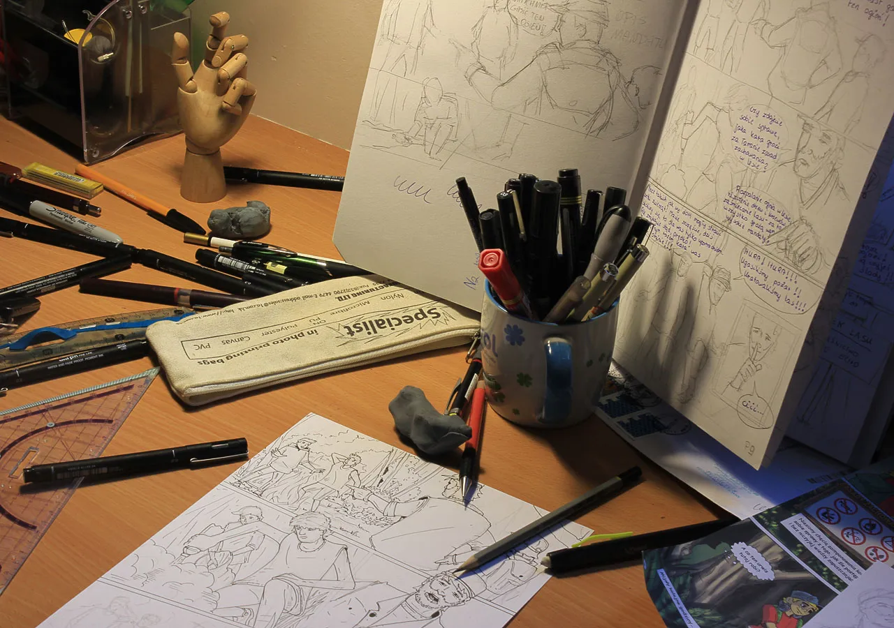 Na biurku artysty widać szkice, ołówki, pisaki i notatki, które pokazują, jak powstaje komiks.