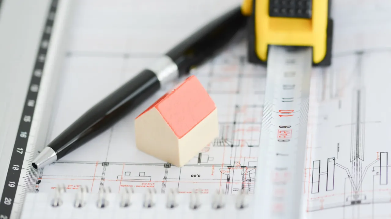 Miniaturka domu, oł&oacute;wek i miarka na planach budowlanych. Pokazuje, ile jest ważne pozwolenie na budowę.