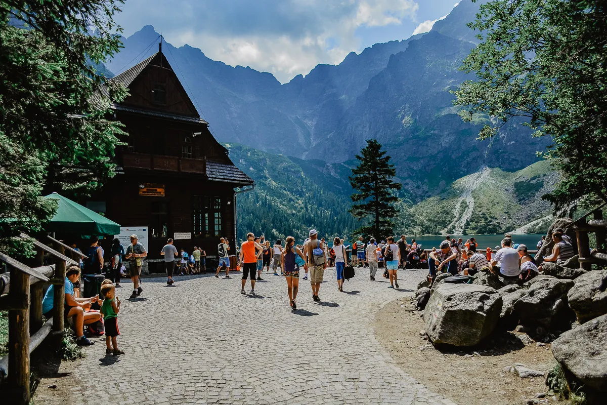 Ludzie odpoczywają przy schronisku nad Morskim Okiem, idealnym miejscu, by zacząć zwiedzanie w Zakopanem. G&oacute;ry Tatry zachwycają.