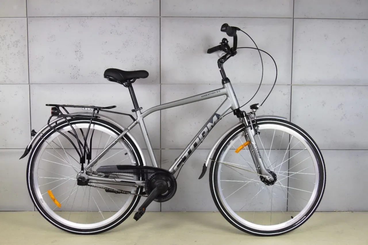 Srebrny rower trekkingowy Storm Marathon 3.0, idealny do 3000 zł, z bagażnikiem i błotnikami, gotowy na miejskie wyprawy.