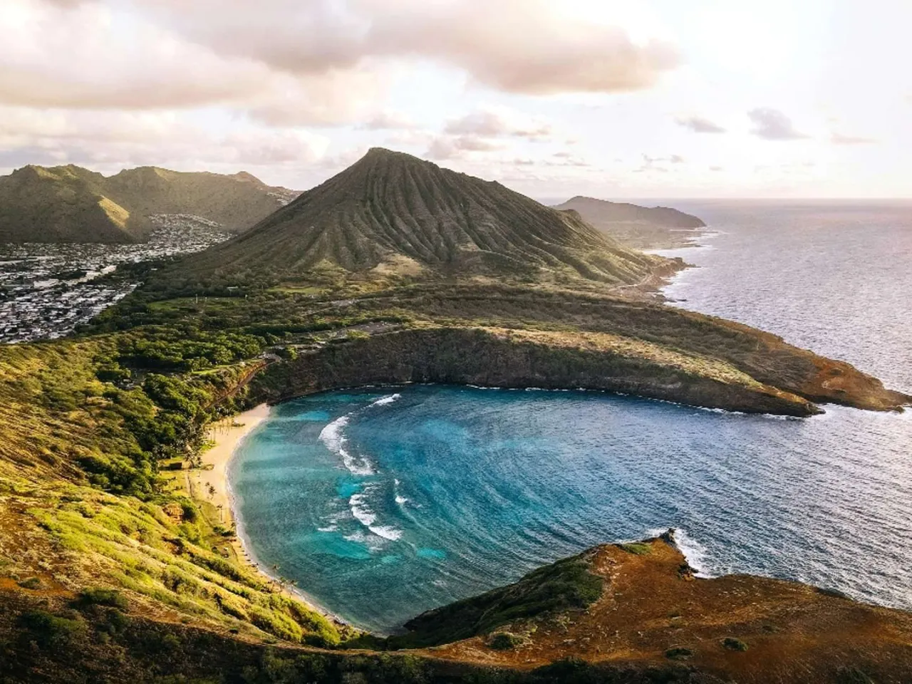 Widok na zatokę z piaszczystą plażą i turkusową wodą, otoczoną zielonymi wzgórzami i górą. To jedno z hawaje najpiękniejsze miejsca.
