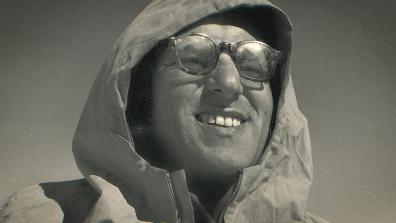 Uśmiechnięty mężczyzna w okularach i kapturze, reżyser zezowatego szczęścia, patrzy w górę.