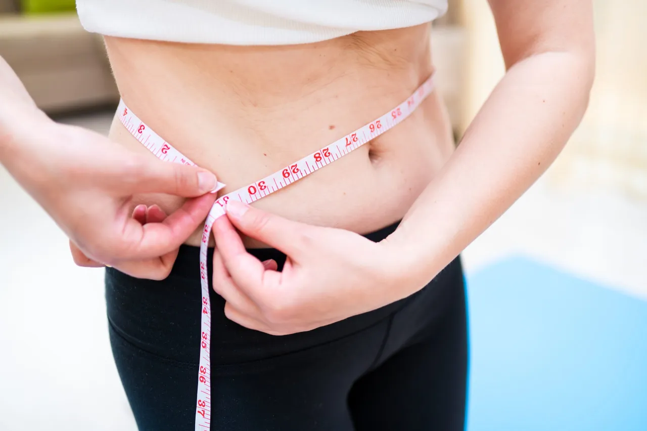 Kobieta mierzy talię centymetrem. Maślan sodu na odchudzanie może pomóc w osiągnięciu wymarzonej sylwetki.