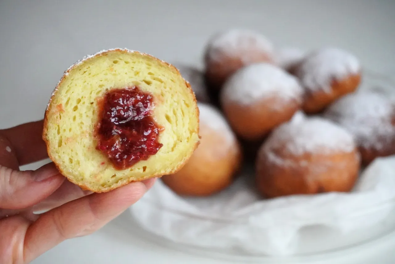 Puszyste pączki z dżemem, posypane cukrem pudrem. Czy pączki są wegańskie? Ten wygląda pysznie!